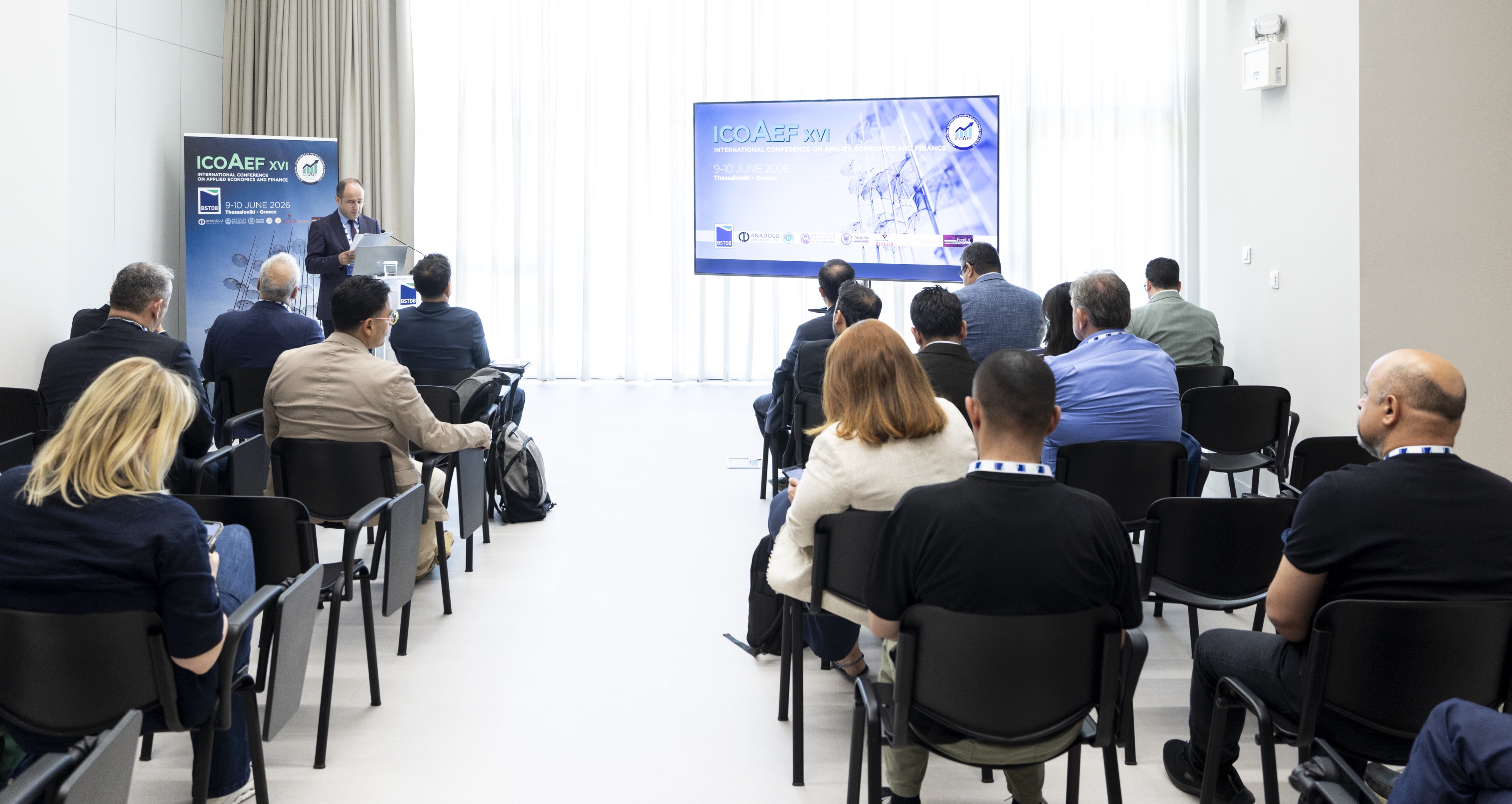 Audience members sit in rows facing a speaker at a podium during a professional conference session.